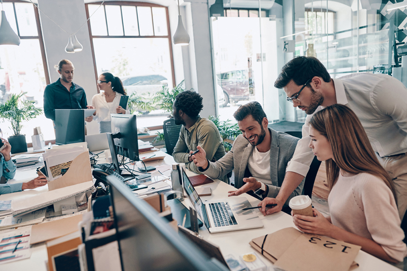 Group of young modern people in smart casual wear communicating and using modern technologies while working in the office